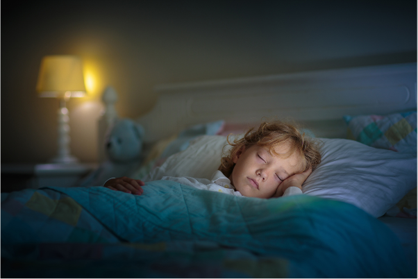 a child asleep in their bed at night, with a dim lamp on in the room